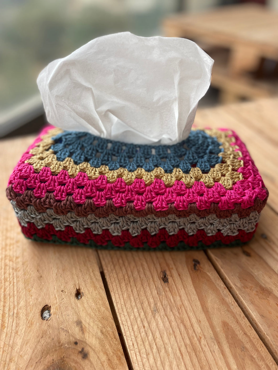 Colorful crocheted tissue box cover with tissues on a wooden surface