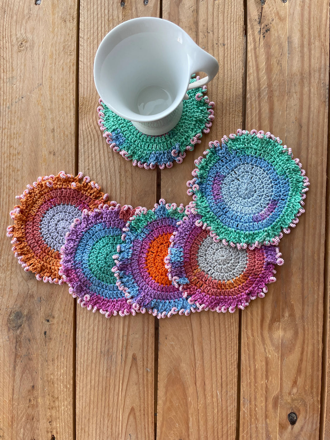 Colorful crocheted coasters on a  surface with a white mug.
