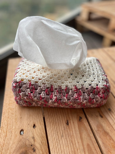 Crocheted tissue box cover with tissues on a wooden surface