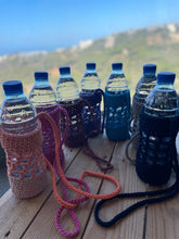 Load image into Gallery viewer, Set of water bottles with colorful knitted covers on a wooden surface with a scenic background.
