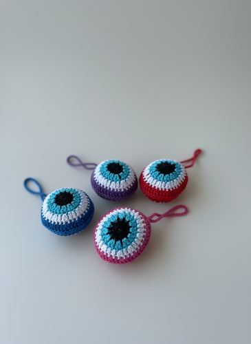 Four crocheted eye-shaped keychains on a wooden surface