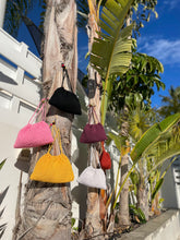 Load image into Gallery viewer, Colorful handbags hanging on a palm tree against a blue sky.
