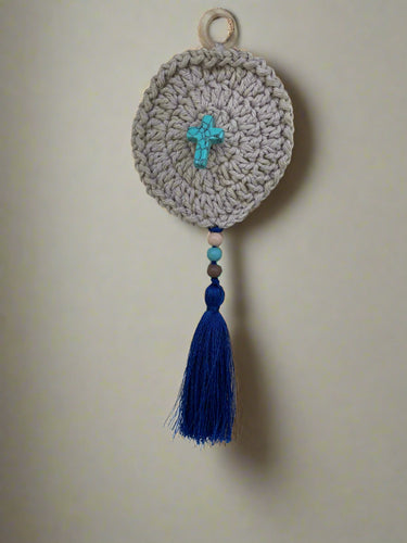 Crocheted round decorative item with a blue tassel on a wall