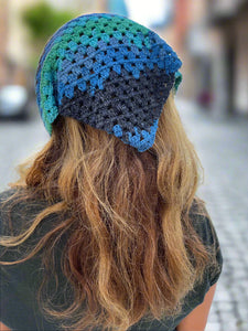 Person wearing a blue and green crocheted headband with blurred outdoor background