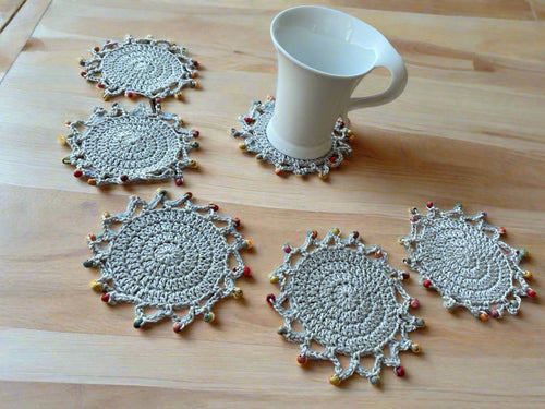 Set of six crocheted coasters on a wooden surface with a mug.