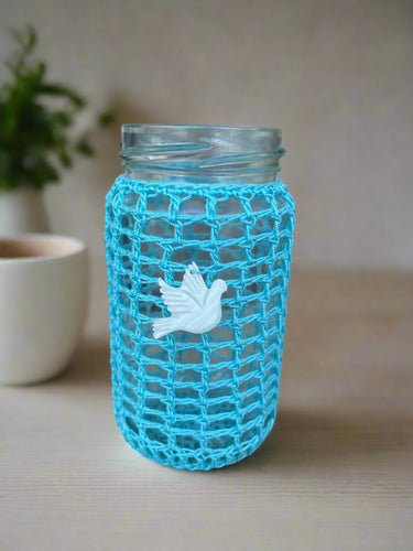 Blue mesh sponge with a white bird design attached to a glass bottle against a concrete background