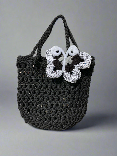 Black crochet bag with a white butterfly design on a textured surface