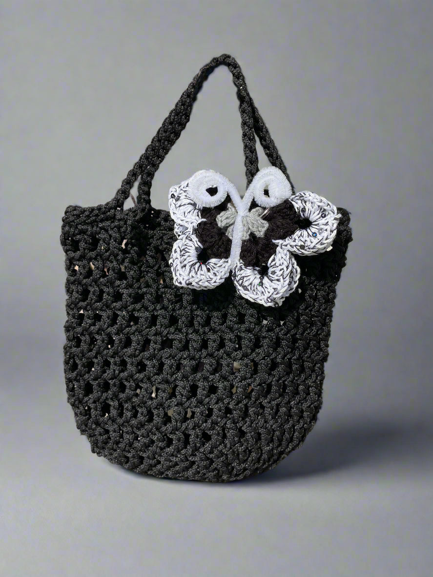 Black crochet bag with a white butterfly design on a textured surface