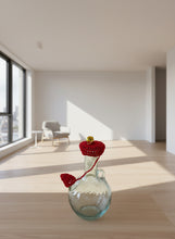 Load image into Gallery viewer, Clear glass bottle with a red crocheted cover and gold bell on a white background
