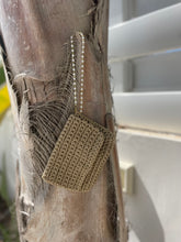 Load image into Gallery viewer, A small beige crocheted pouch with a pearl-bead chain strap, hanging on a textured tree trunk outdoors.
