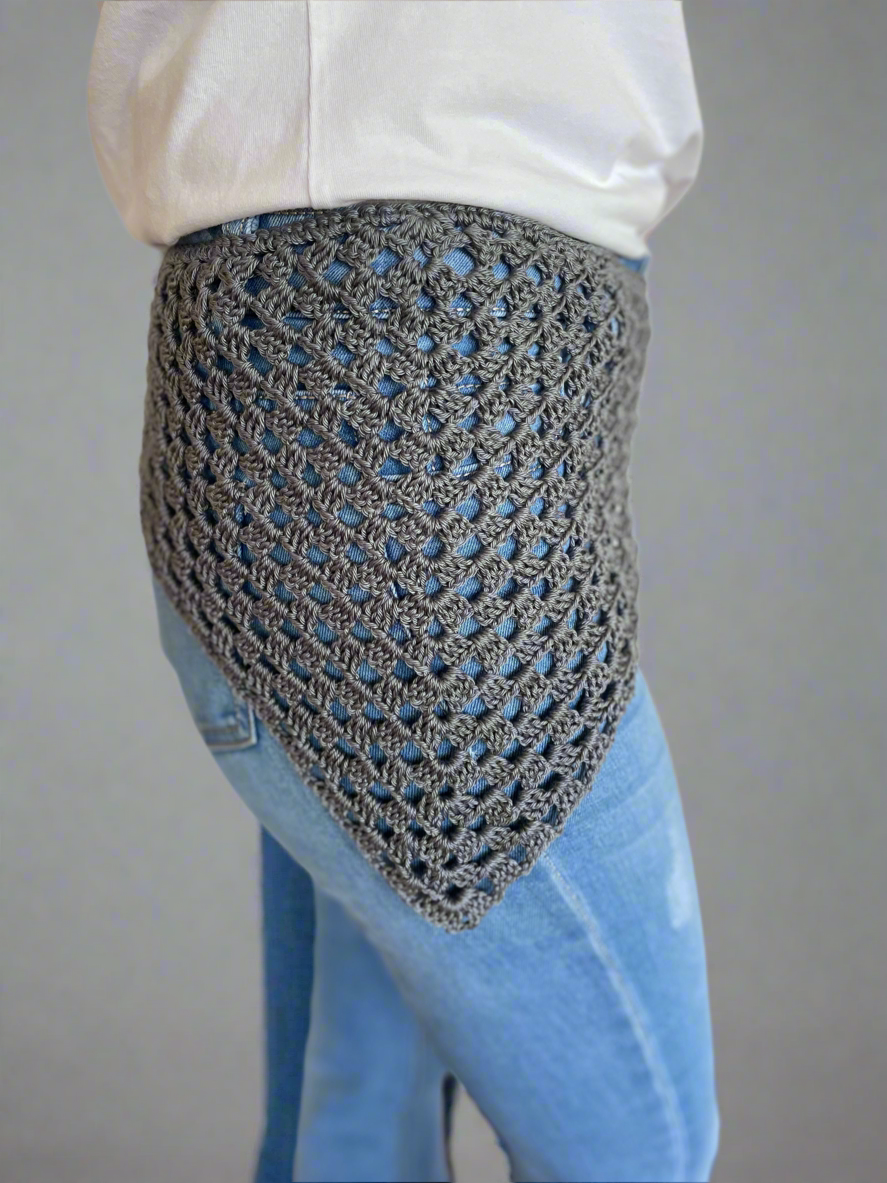 Person wearing a textured gray shawl over a white shirt and blue jeans on a plain background