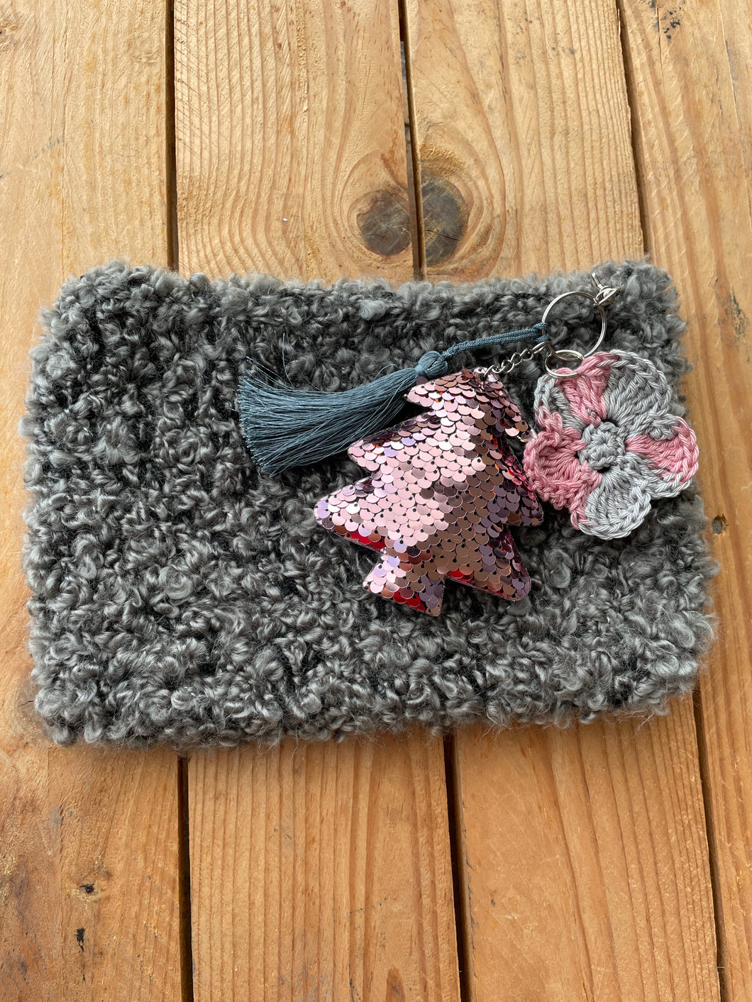 Gray textured pouch with decorative keychain on a wooden surface