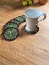 Load image into Gallery viewer, Green crocheted coasters on a wooden surface with a white mug.
