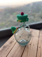 Load image into Gallery viewer, Clear glass bottle with a green knitted cap on a wooden surface with a blurred natural background
