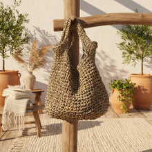 Load image into Gallery viewer, Woven bag on a wooden surface with a plant in the background
