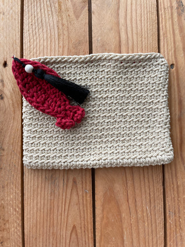Knitted pouch with a red and black decorative item on a wooden surface