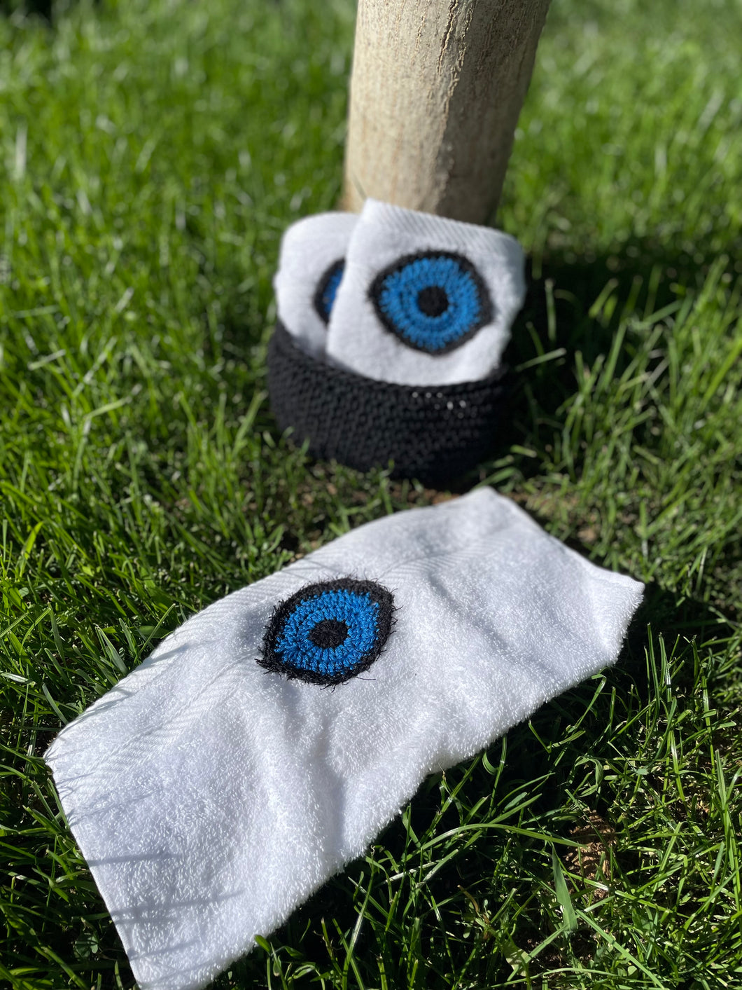 Crocheted eye pattern on a white sock and black bandana on grass