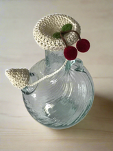 Load image into Gallery viewer, Clear glass bottle with a crocheted top and ears on a light wooden surface
