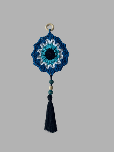 Blue crocheted decorative item with beads and a tassel on a gray background