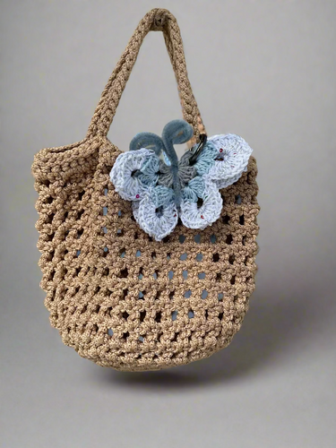 Crocheted bag with butterfly decoration hanging on a tree branch