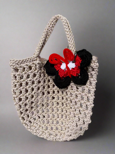Beige crochet bag with a decorative bow attached, placed on a wooden surface.