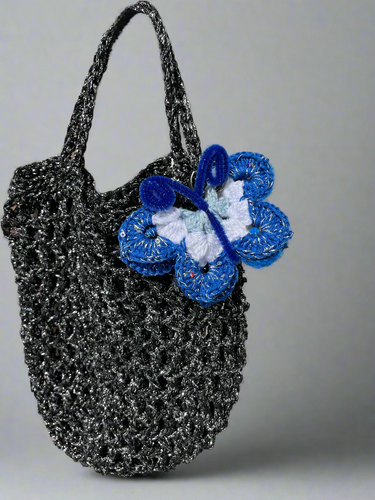 Black textured handbag with blue and white crochet butterfly against a natural background