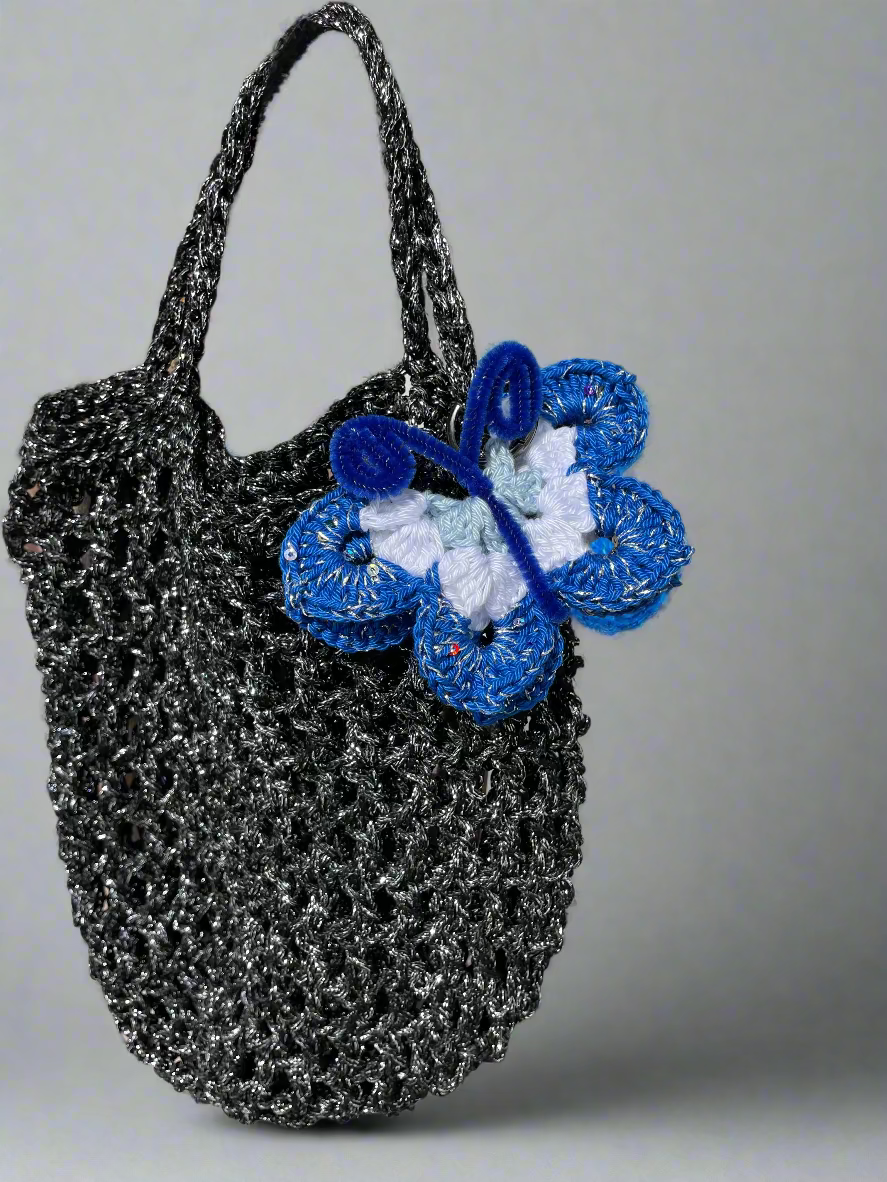 Black textured handbag with blue and white crochet butterfly against a natural background