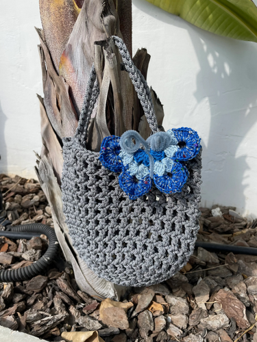 Gray crochet bag with blue butterfly decoration on a natural background