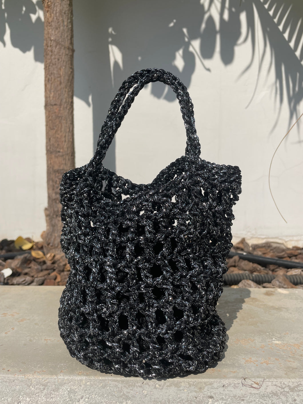 Black textured handbag leaning against a wall with plants in the background