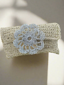 Beige clutch bag with a silver floral brooch on green foliage