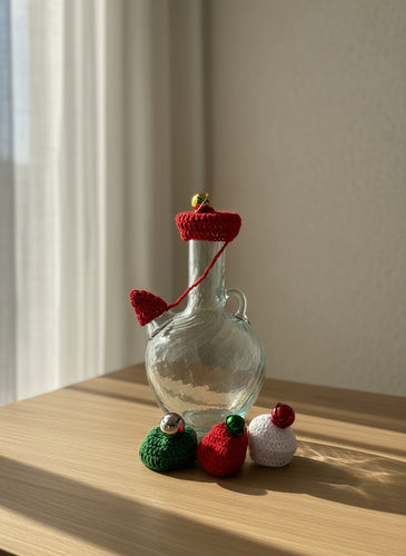 Glass bottle with crocheted red cap and decorative elements on a light gray background