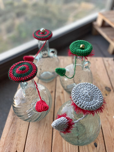 Decorative glass bottles with crocheted covers on a wooden surface.