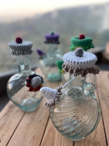 Glass bottles with crochet lids on a wooden surface outdoors