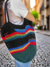 Load image into Gallery viewer, Person holding a black crochet bag with colorful stripes on a blurred street background
