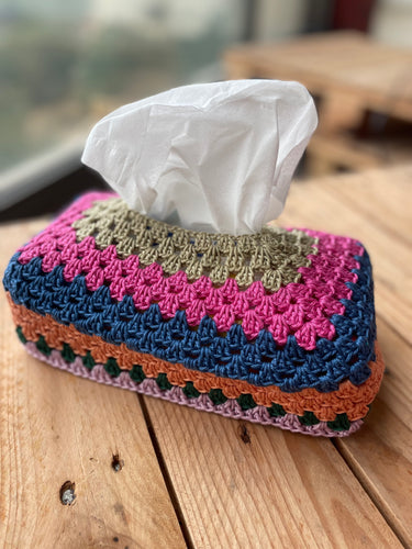 Colorful crocheted tissue box cover with tissues on a wooden surface