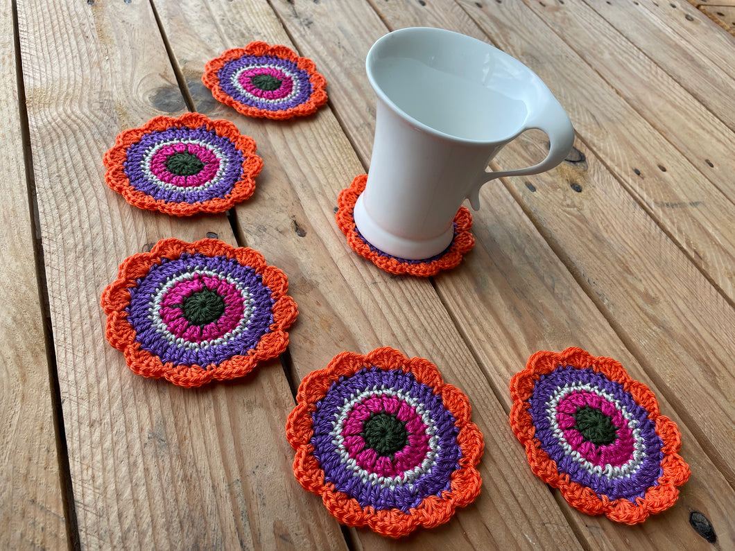 Set of colorful crocheted coasters on a wooden surface with a white mug.