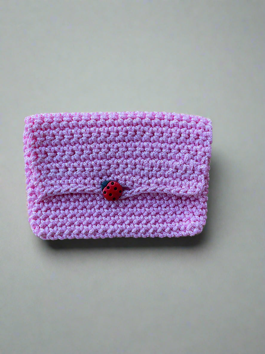 Pink knitted pouch with a ladybug on a wooden surface