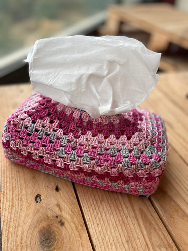 Pink and gray striped crochet tissue box cover with tissues on a wooden surface