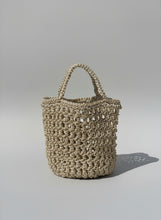 Load image into Gallery viewer, Woven handbag against a neutral wall with plant shadows
