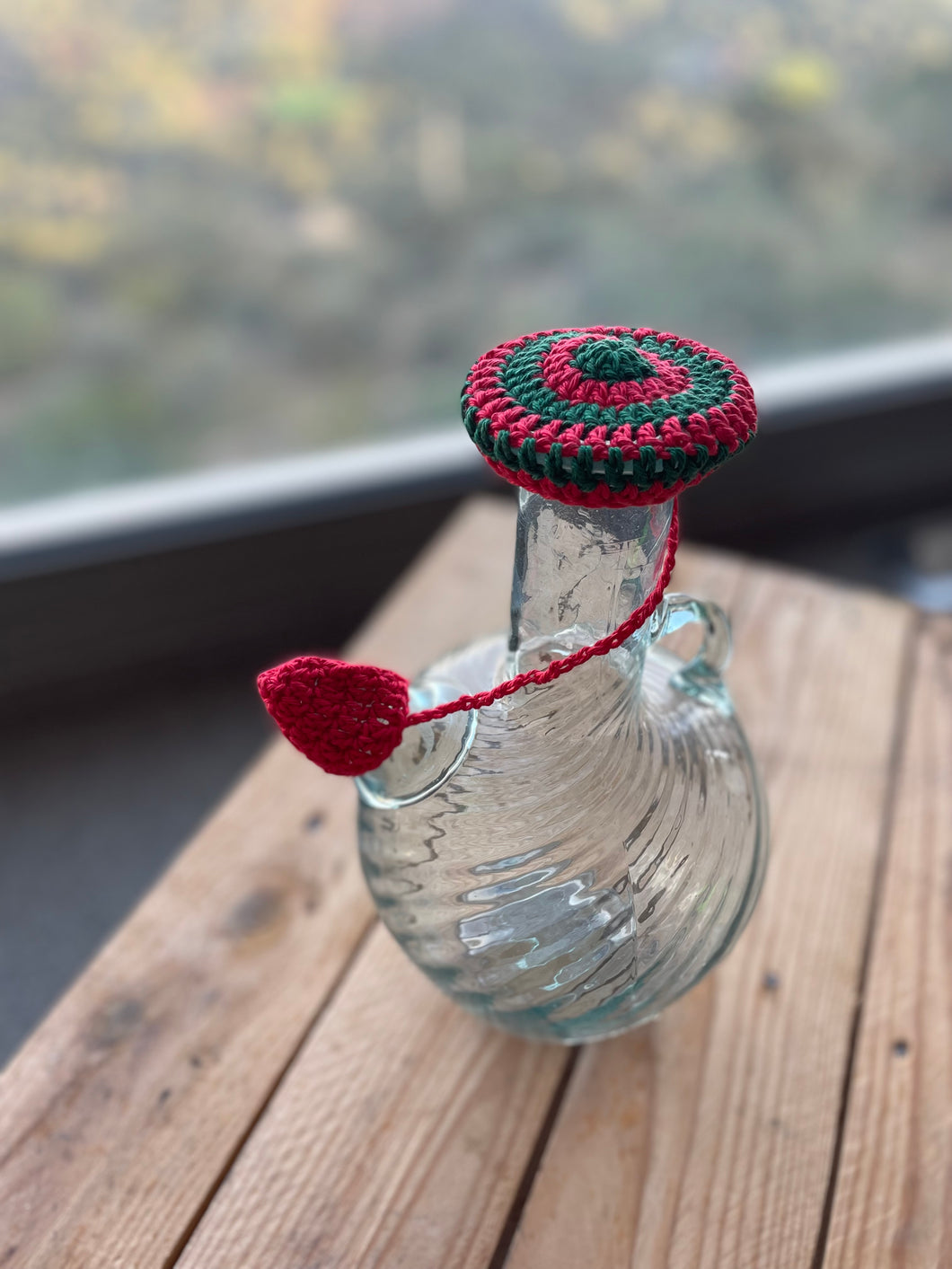 Glass bottle with a crocheted red and green lid on a wooden surface