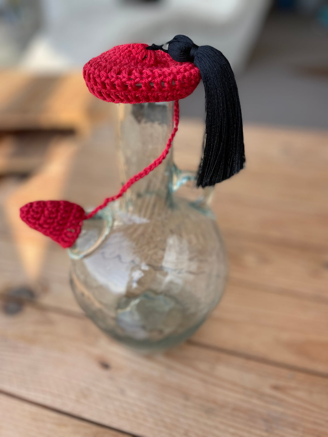 Glass bottle with a red and black knitted heart and tassel on a wooden surface