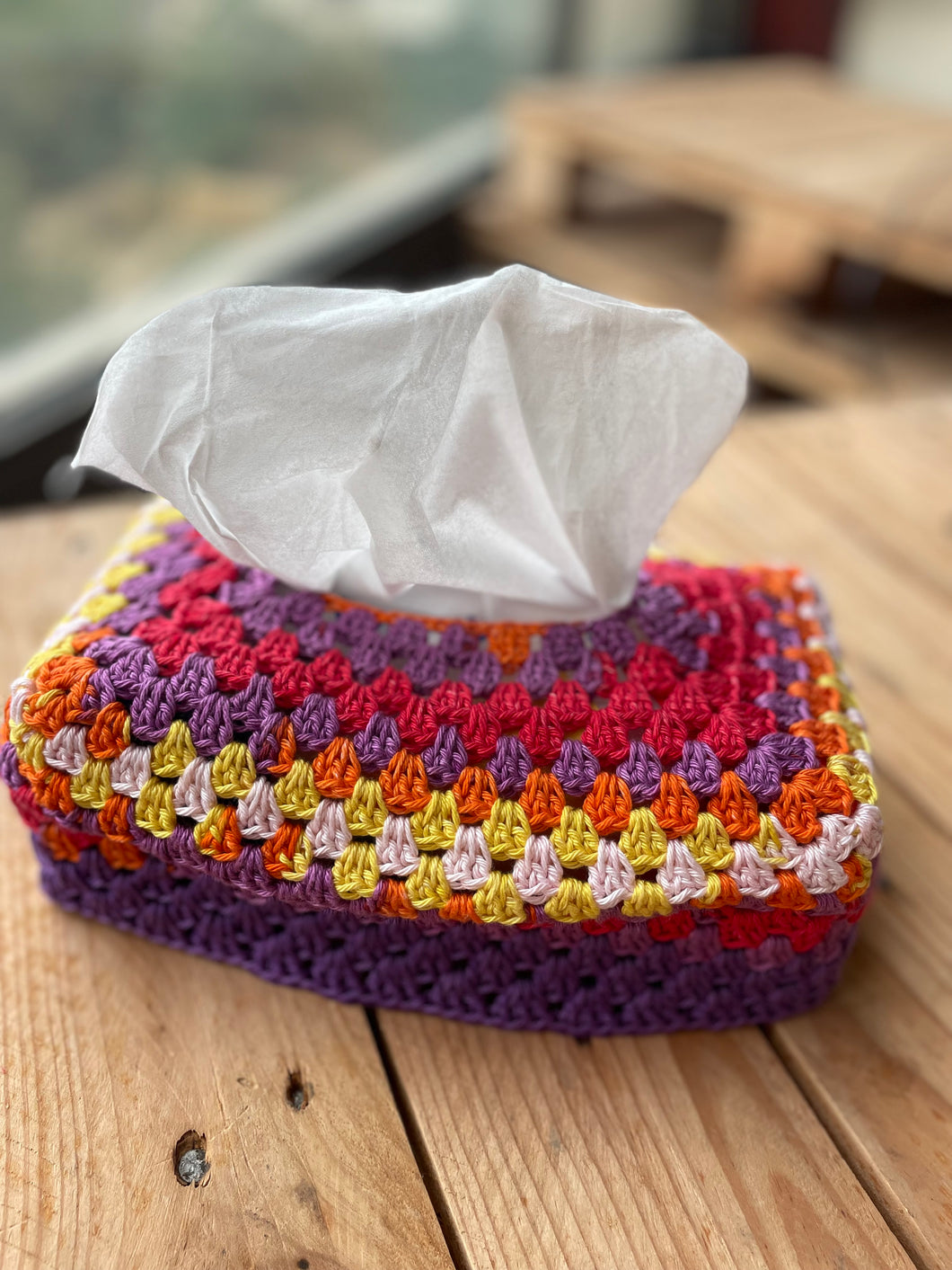 Colorful crocheted tissue holder with tissues on a wooden surface