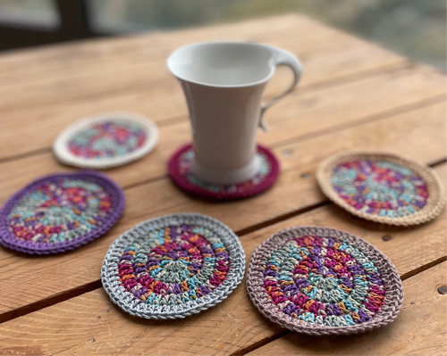 Colorful crocheted coasters on a wooden table with a white mug.