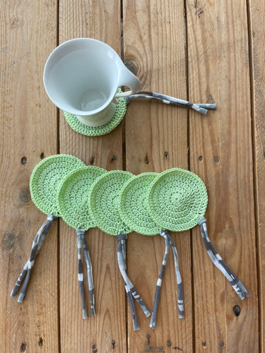 Green crocheted coasters with hairpins on a wooden surface