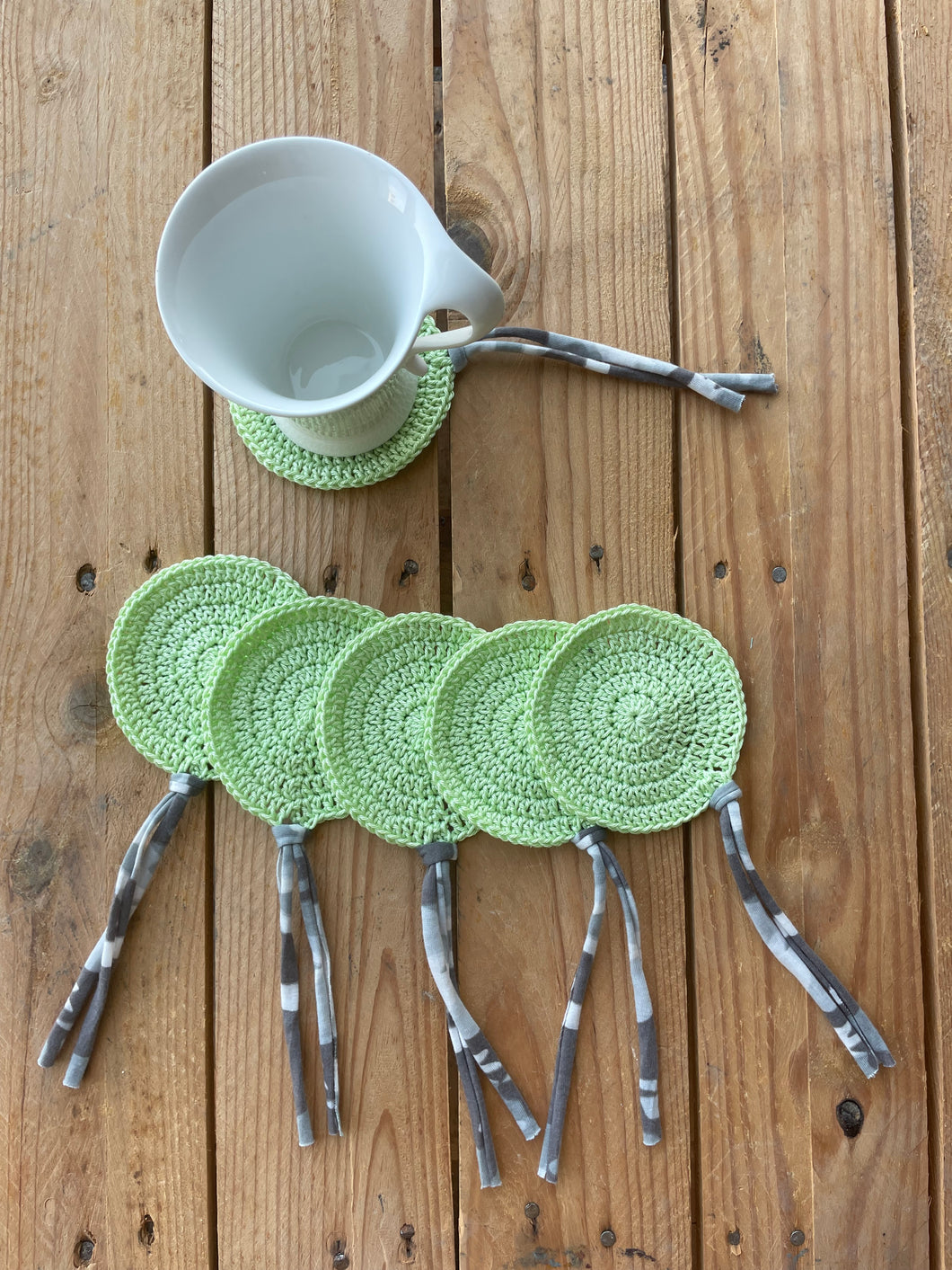 Green crocheted coasters with hairpins on a wooden surface
