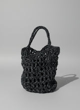 Load image into Gallery viewer, Black textured handbag leaning against a wall with plants in the background
