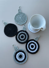 Load image into Gallery viewer, Set of crocheted coasters with circular patterns on a wooden surface with a white mug.
