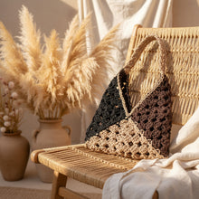 Load image into Gallery viewer, A handmade crocheted shoulder bag in three colors: black, dark brown, and beige. The bag is photographed hanging against a white exterior wall with a glimpse of palm trees and blue sky in the background.
