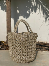 Load image into Gallery viewer, Woven handbag against a neutral wall with plant shadows

