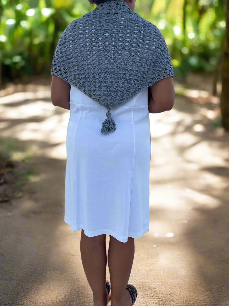 Person wearing a gray crocheted shawl over a white dress in a natural setting